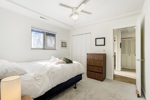 Ein Schlafzimmer mit einem Bett, einem Deckenventilator, einem Fenster, einem Kleiderschrank und einer Tür zu einem anderen Raum.