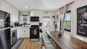Une cuisine moderne avec des meubles blancs, une cuisinière noire et une table à manger en bois, accompagnée de bancs.