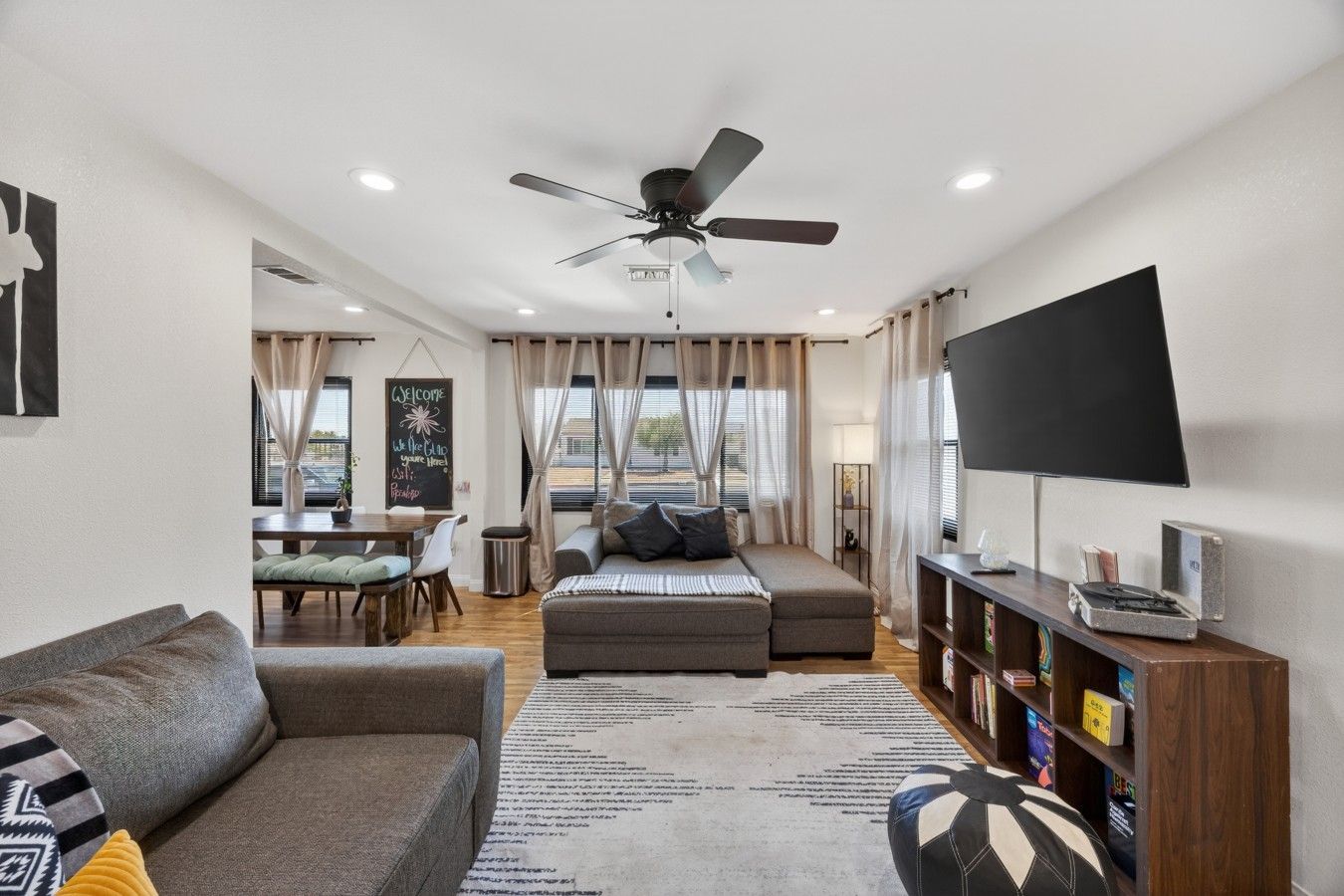 A modern living room with a sofa, a dining table, a TV, and a ceiling fan.