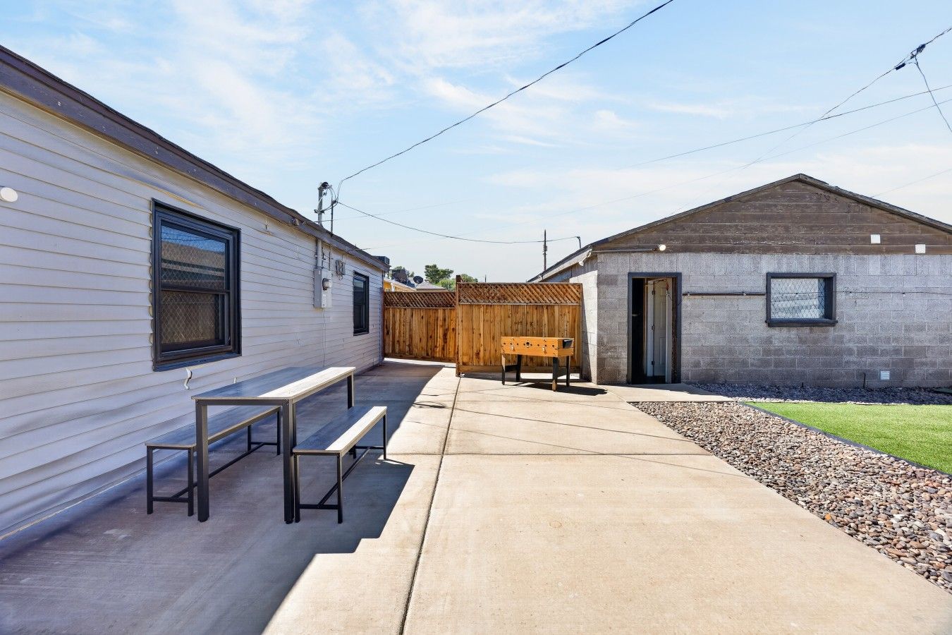 Un quartier résidentiel comprenant une terrasse en béton, des bancs en bois, un petit bâtiment doté d’une porte et une clôture en bois.