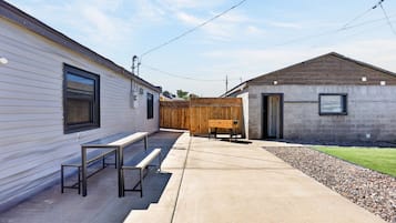 Un quartier résidentiel comprenant une terrasse en béton, des bancs en bois, un petit bâtiment doté d’une porte et une clôture en bois.