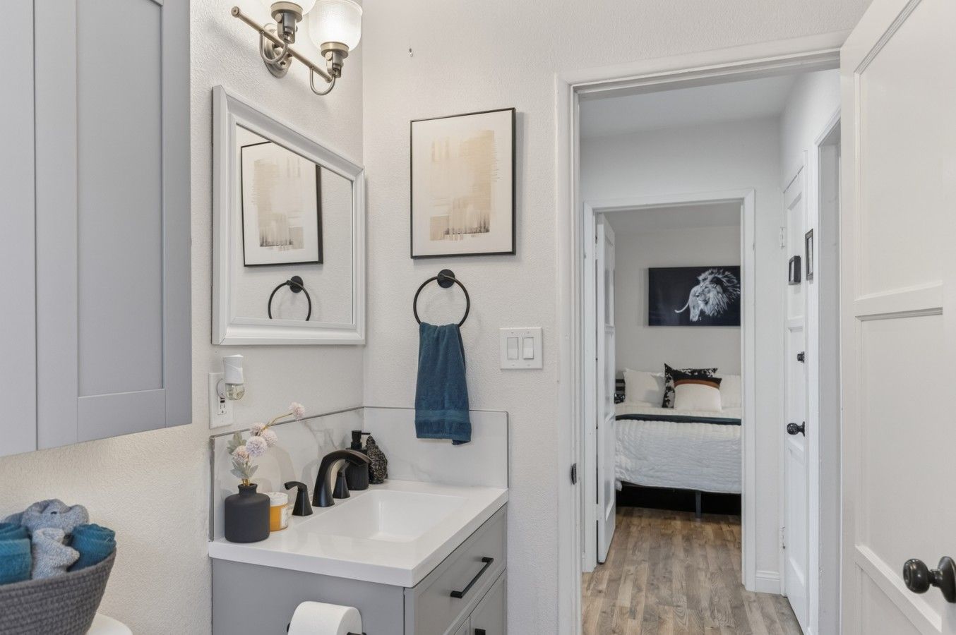 Un bagno con un mobile lavabo bianco, uno specchio, un appendi asciugamani e un quadro incorniciato al muro.