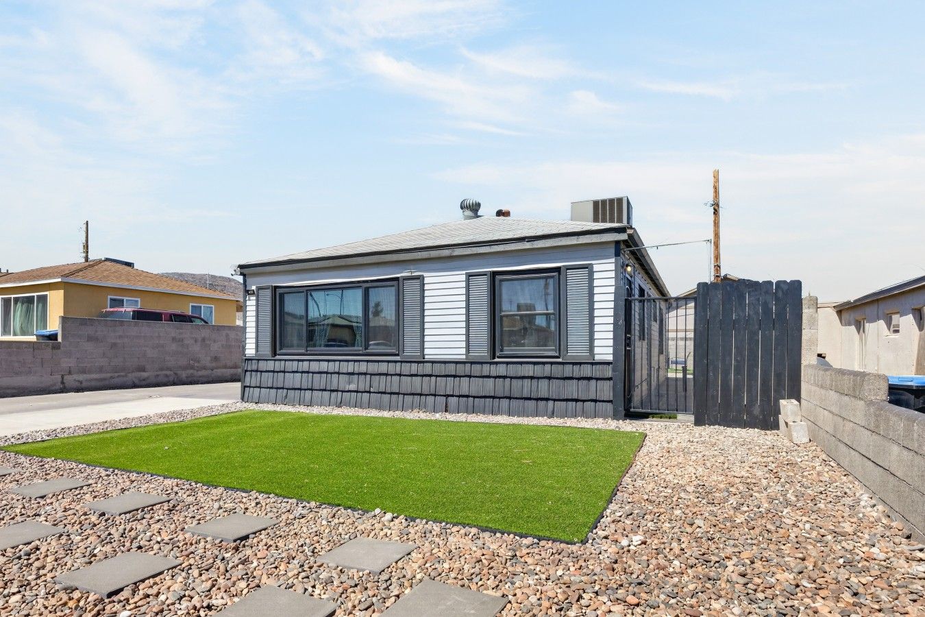 Une maison de plain-pied avec un petit jardin devant, une allée pavée et une clôture en bois.