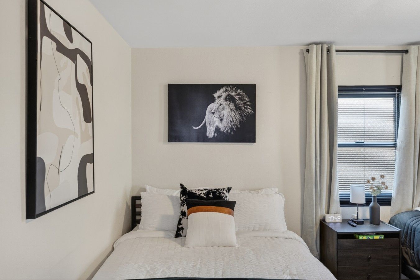Une chambre à coucher avec un lit, une table de chevet, une horloge murale et une fenêtre avec des rideaux.