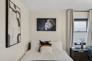 Ein Schlafzimmer mit Bett, Nachttisch, Wanduhr und Fenster mit Vorhängen.
