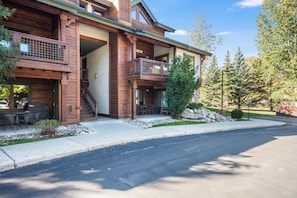 A multi-story wooden building with a balcony, a covered outdoor seating area, and a stone wall. - Ground Floor - No Stairs Required - Professionally Decorated & Furnished (Steamboat Springs)
