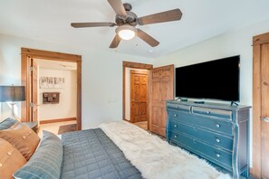 Ein Schlafzimmer mit Deckenventilator, Fernseher, Kommode und einem Bett mit flauschigem Teppich.