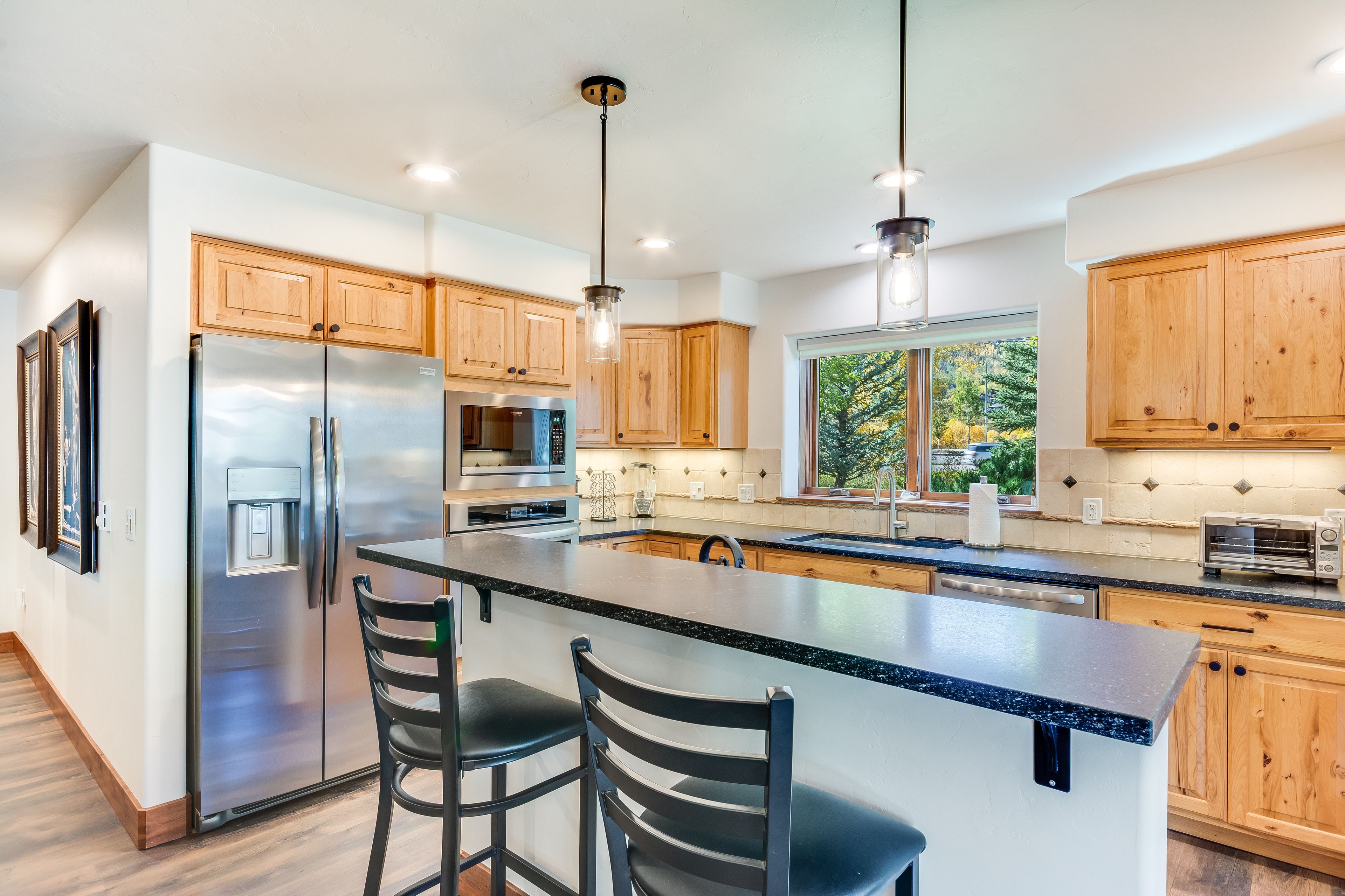 A modern kitchen with stainless steel appliances, wooden cabinets, a large island with bar stools, and pendant lighting.