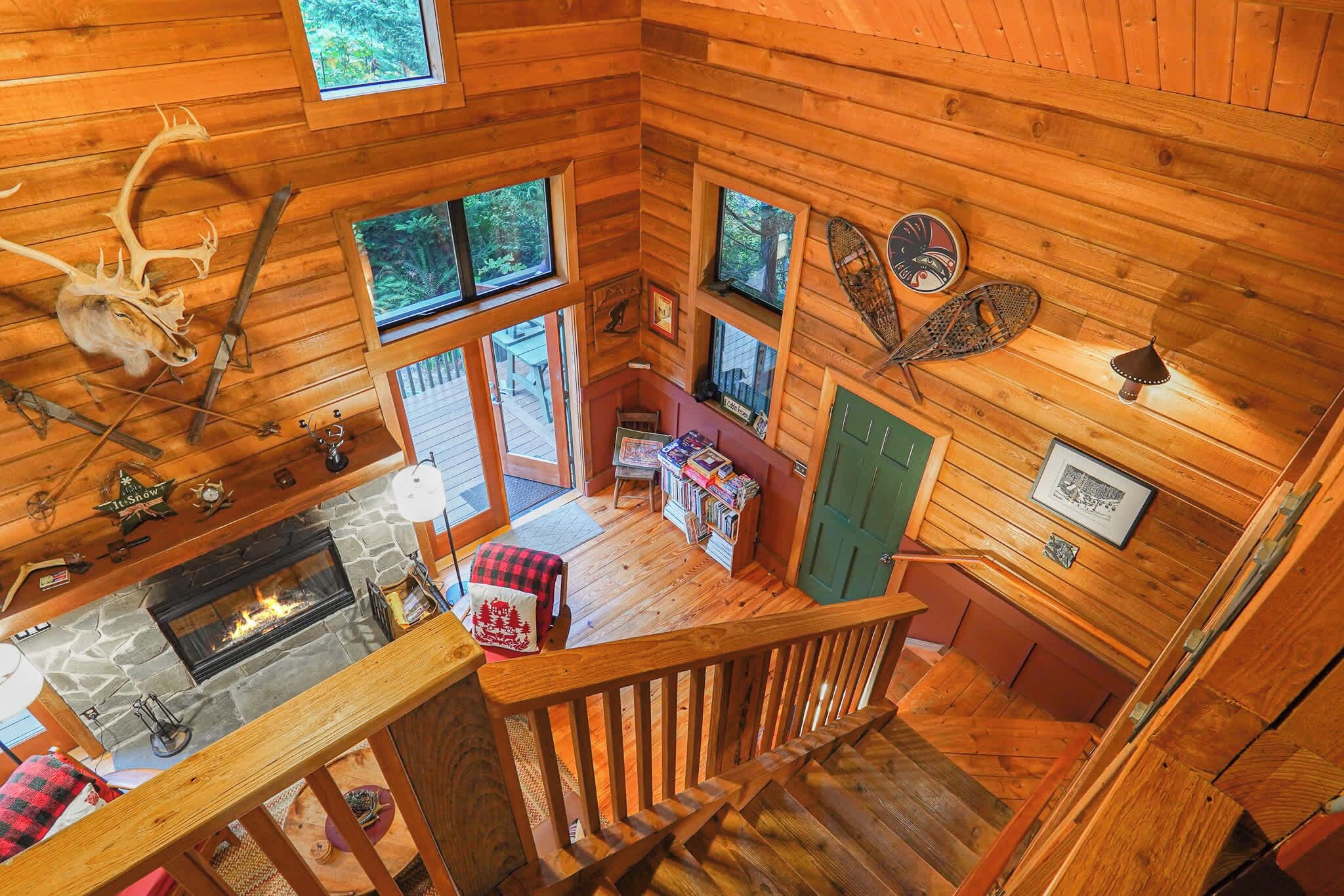 A cabin interior with a stone fireplace, wooden walls, and a loft area with a view of the outdoors.
