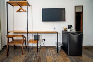 Huoneessa on puinen työpöytä, tuoli, seinälle asennettu televisio ja kahvinkeitin.
