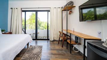 A hotel room with a bed, a desk, a television, and a view of palm trees through the sliding glass door.