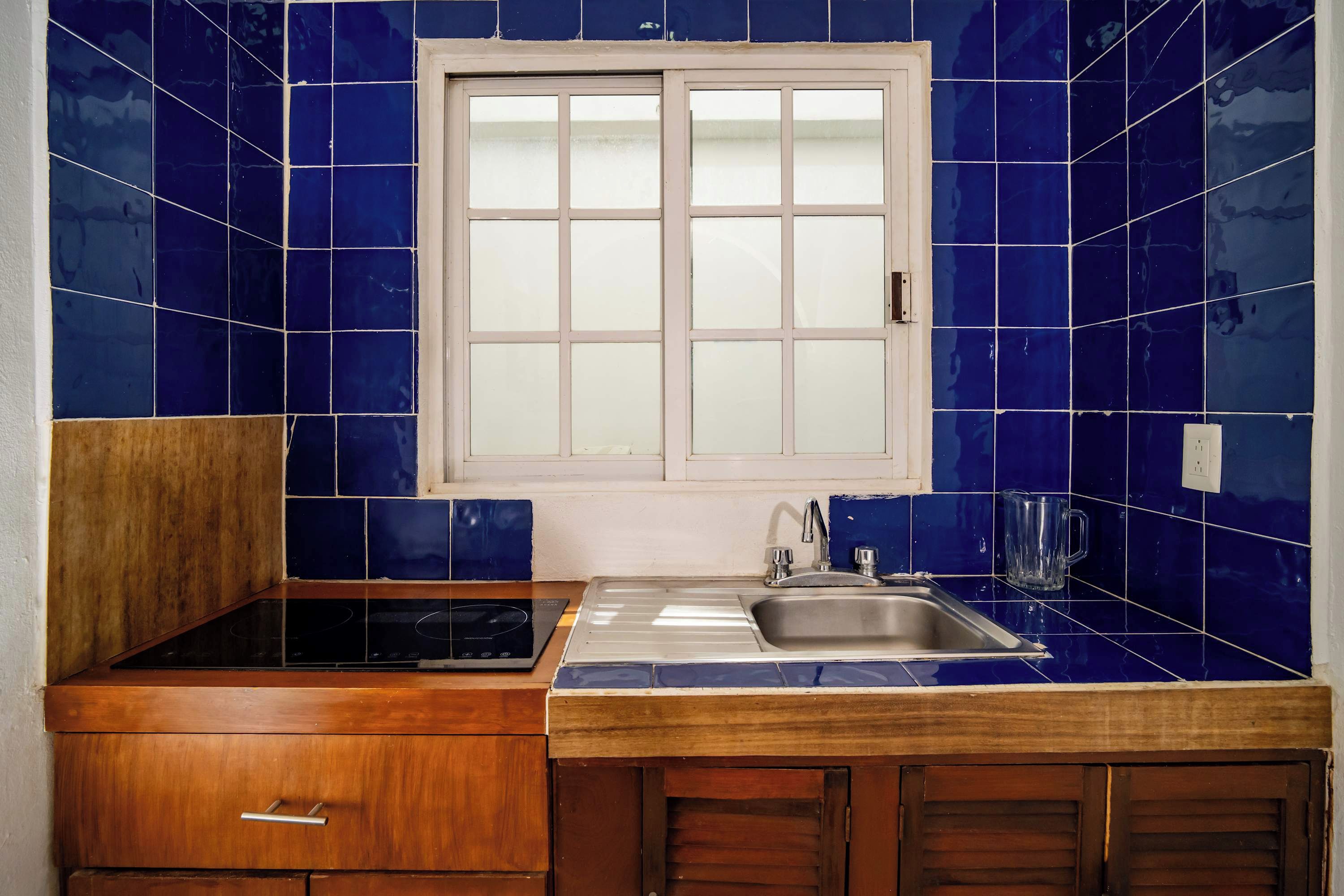 Een keuken met blauwe tegels, een raam, een spoelbak en houten kastjes.