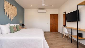 A bedroom with a bed, a desk, a chair, a TV, and an air conditioning unit.