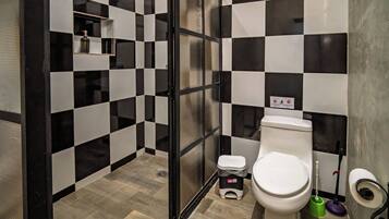 Ein Badezimmer mit Wand in Schwarz-Weiß-Karos, einer weißen Toilette, einem Mülleimer und einer Duschkabine mit Glastür.