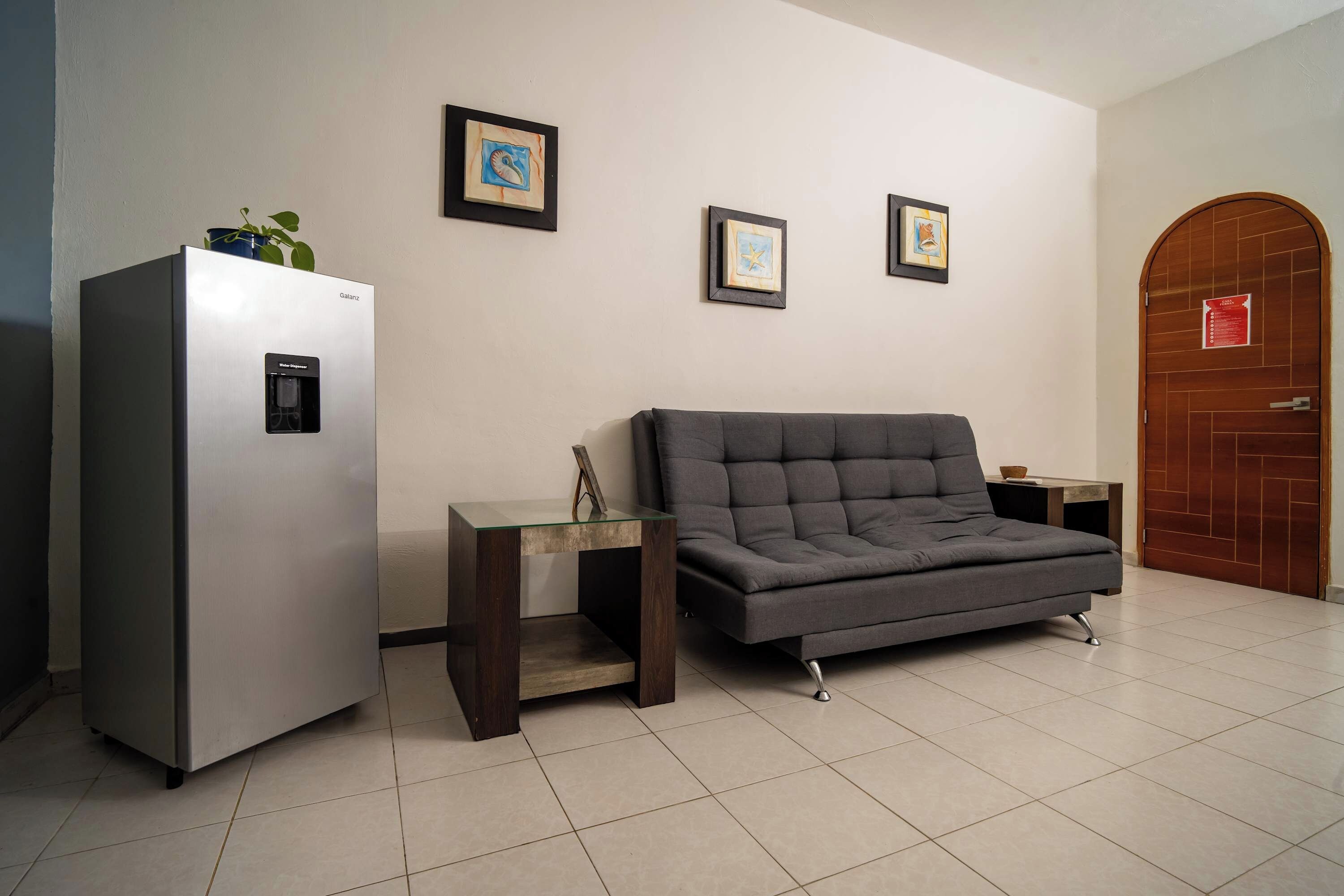 A modern living room with a gray sofa, a refrigerator, and a wooden door.