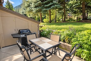 Eine Terrassenanlage im Freien mit Grill, Tisch und Stühlen.