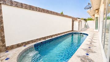 A swimming pool with a stone wall and tiled floor, surrounded by a building with a glass door.
