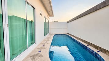 A swimming pool with a tiled edge, adjacent to a building with large glass doors and a white exterior wall.