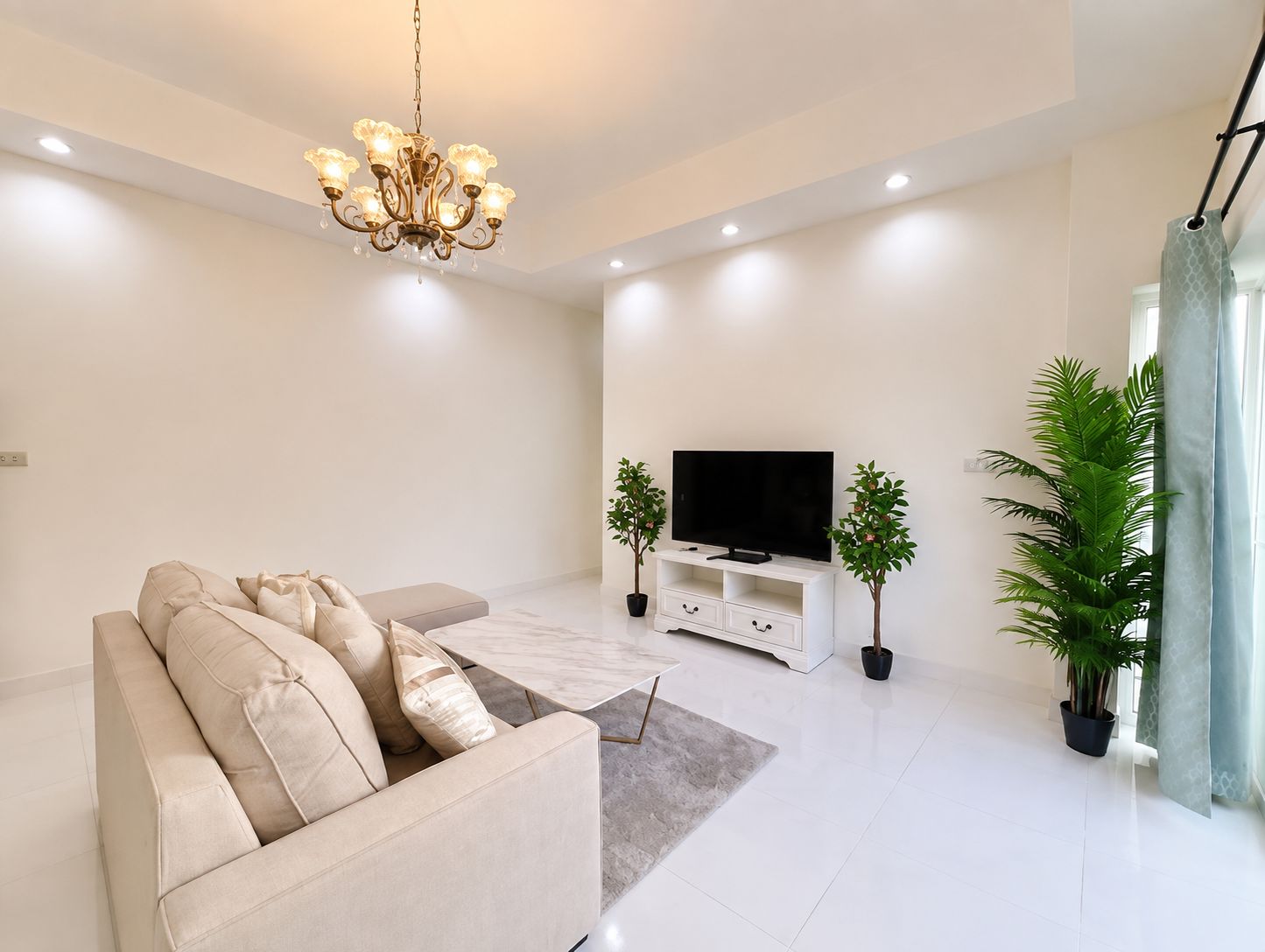 A modern living room with a sofa, a flat-screen TV, a chandelier, and potted plants.