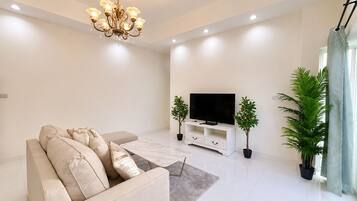 A modern living room with a sofa, a flat-screen TV, a chandelier, and potted plants.