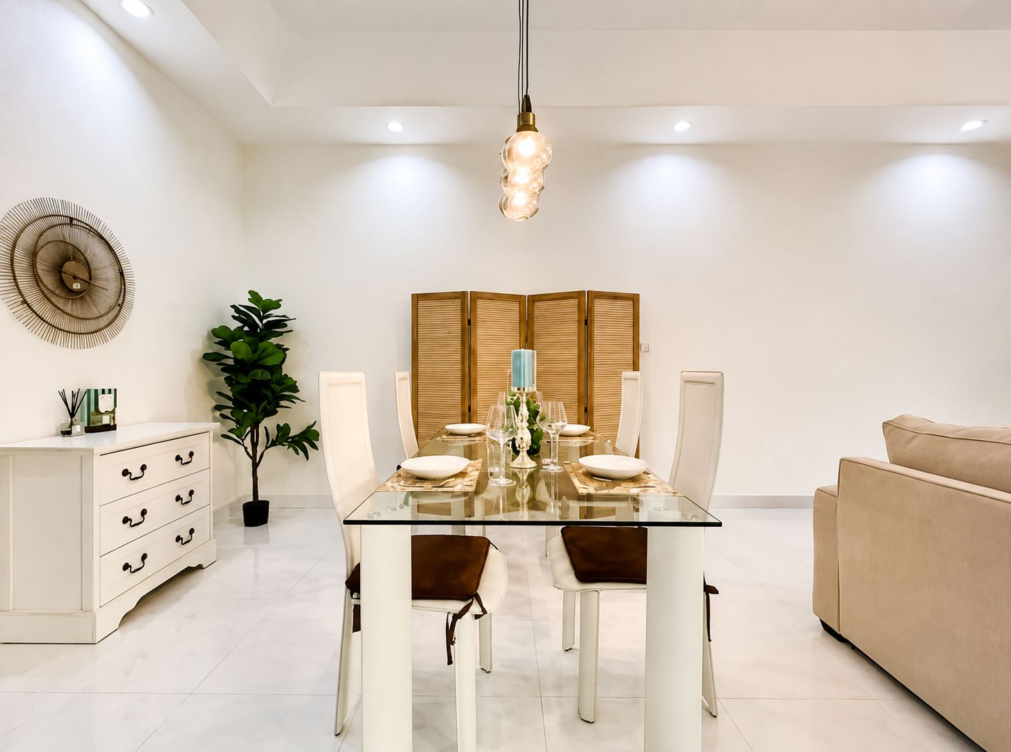 A modern dining area with a glass table, white chairs, and a beige sofa.