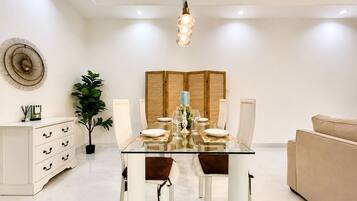 A modern dining area with a glass table, white chairs, and a beige sofa.