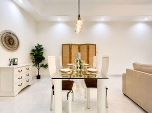 A modern dining area with a glass table, white chairs, and a beige sofa. - Private Pool Villa Pattaya  2BR • 2BA (Pattaya)