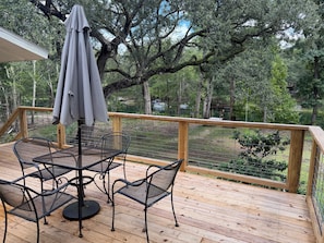 Une terrasse en bois, agrémentée d’une table et de chaises, entourée d’une balustrade en bois, et offrant une vue sur une zone boisée.