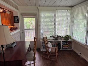 A cozy room with a wooden floor, a dining table with chairs, a rocking chair, a window with blinds, and a door leading outside. - Rivendell Springs River Home: 12 Private Acres on Santa Fe River near Springs (High Springs)