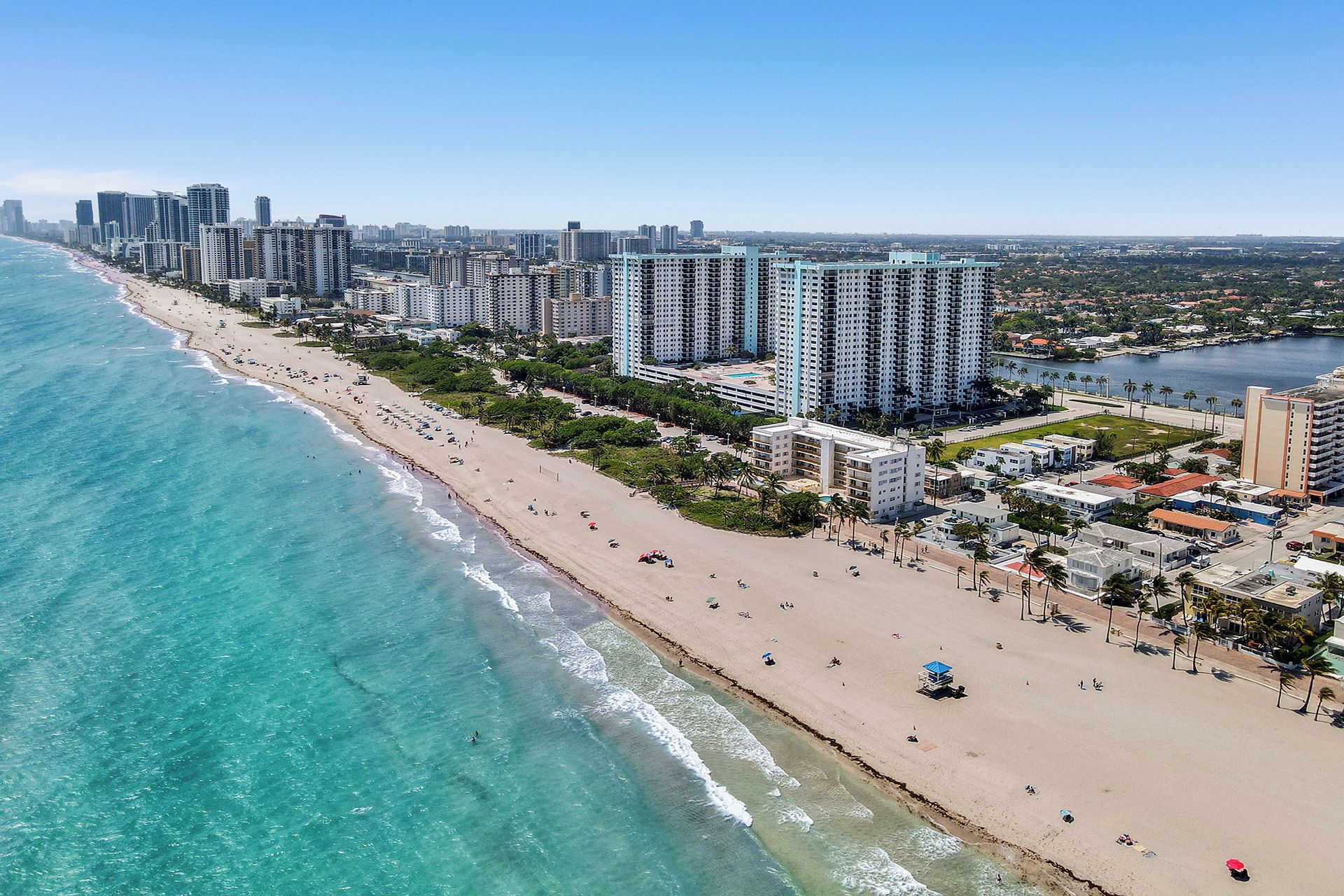A coastal cityscape with high-rise buildings, a sandy beach, and a clear blue sea.