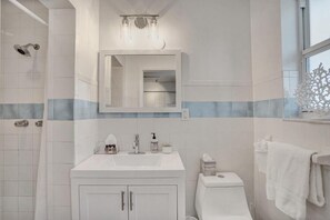Ein Badezimmer mit weißem Waschbecken, Spiegel und Toilette, mit einer Duschkabine links.