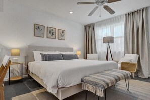 Een slaapkamer met een bed, nachtkastjes, een stoel, een vloerlamp en een plafondventilator.