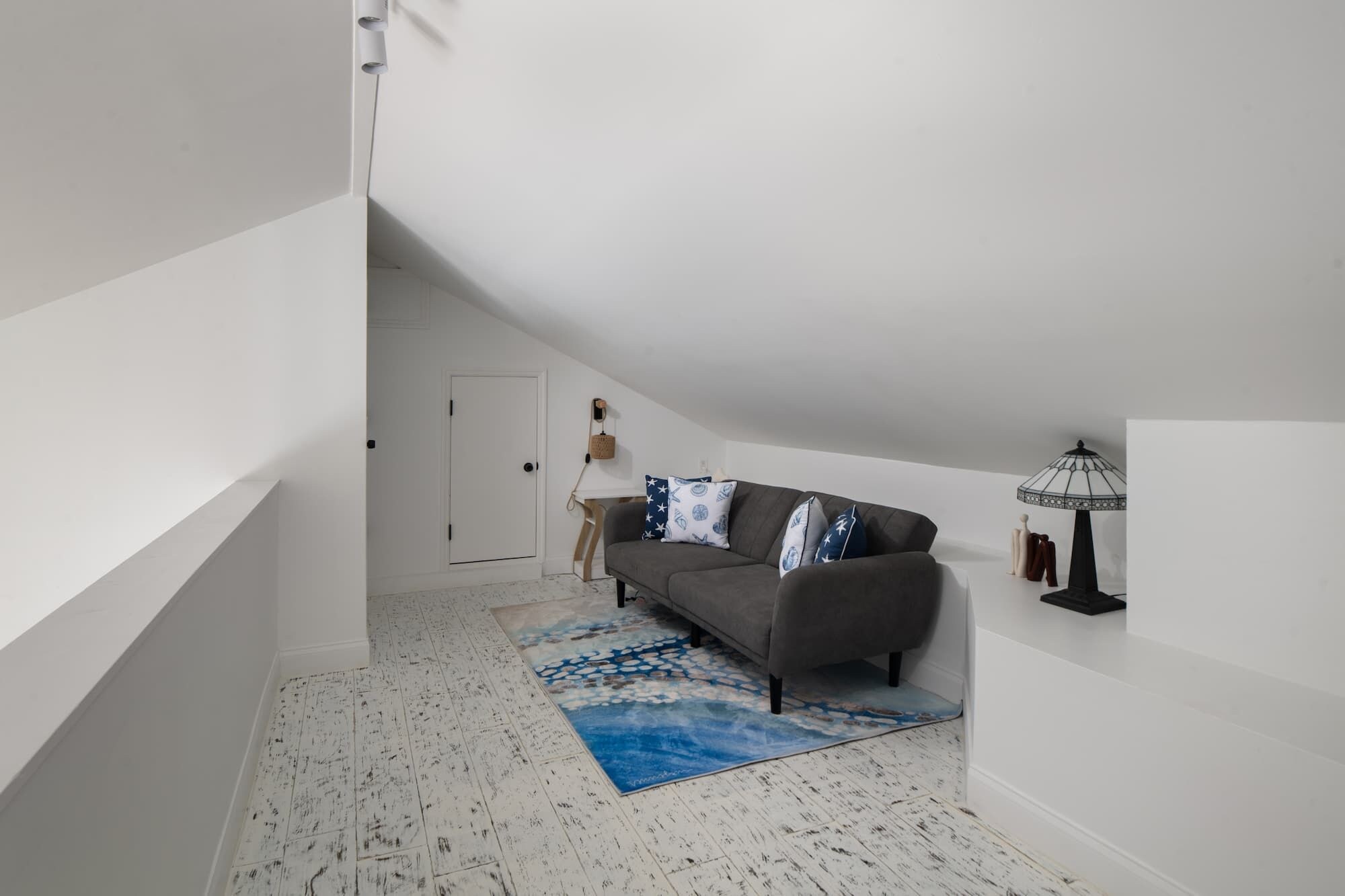 A room with a gray sofa, a patterned rug, a door, and a lamp.