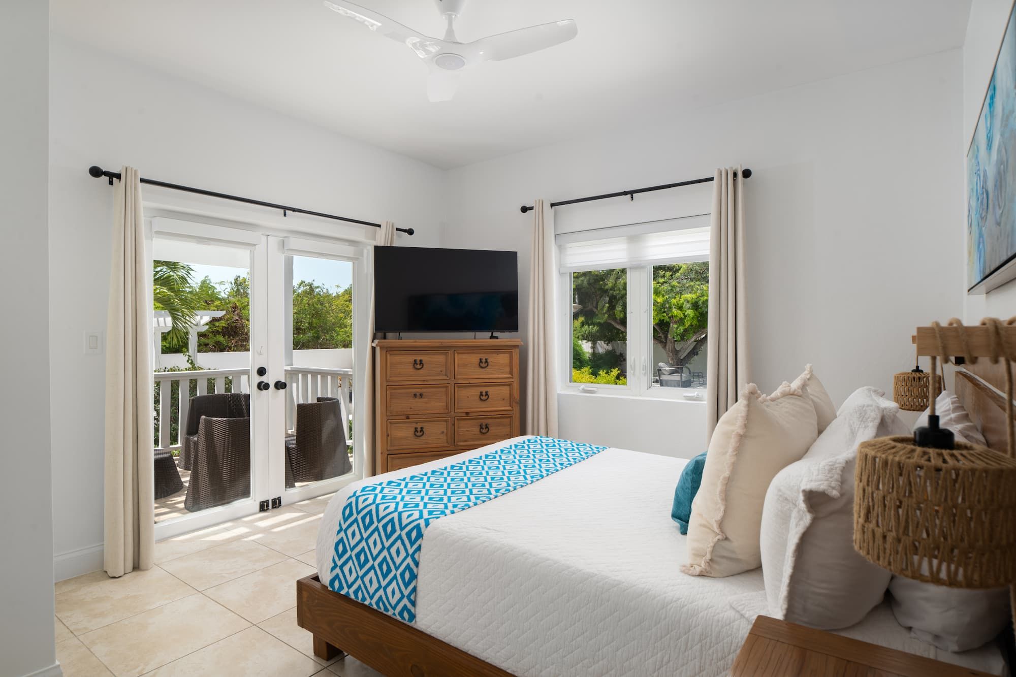A bedroom with a bed, a dresser, a television, and a balcony.