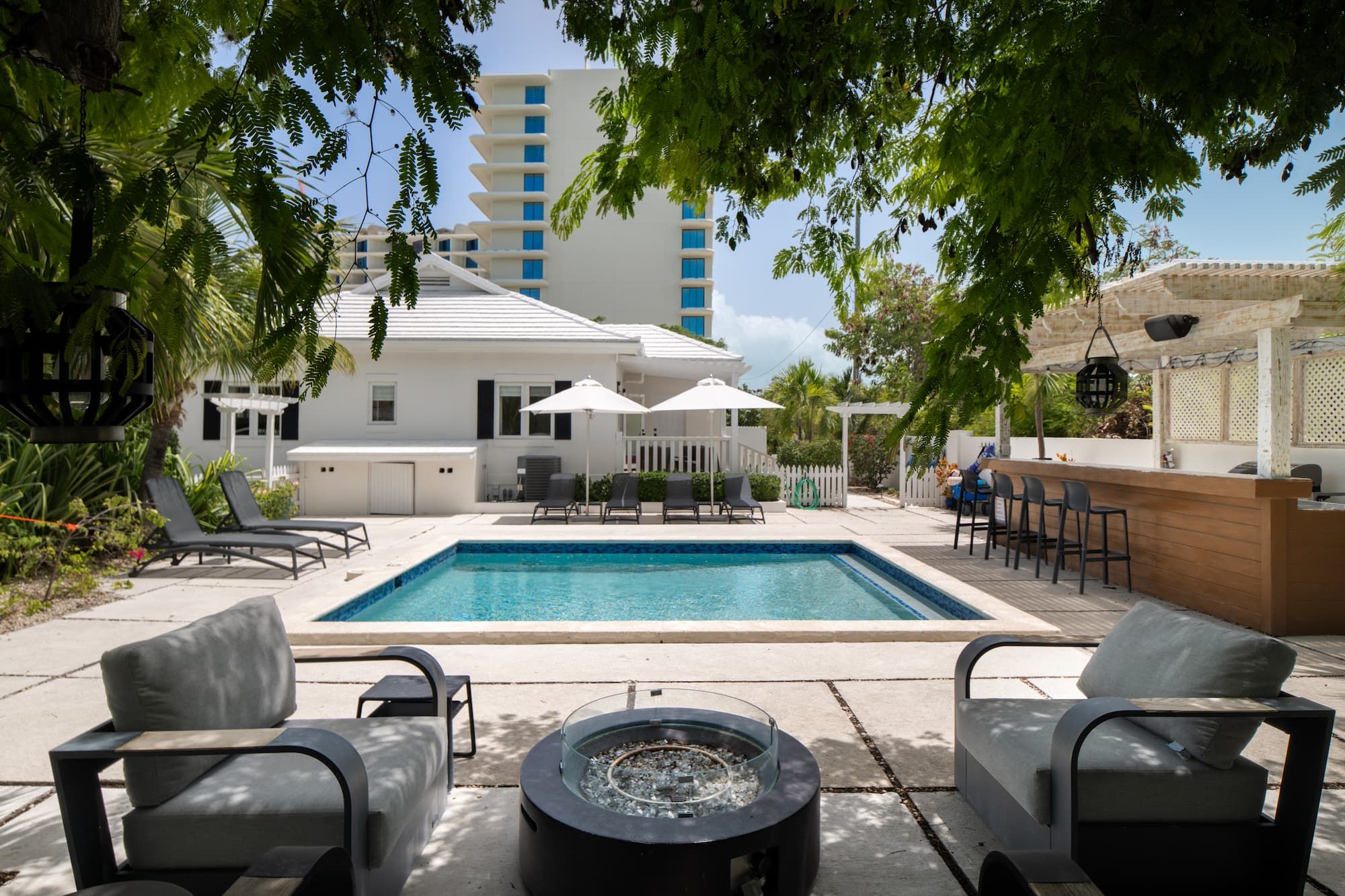 Un espace piscine avec des chaises longues, un foyer et un coin bar.