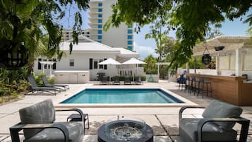 Un espace piscine avec des chaises longues, un foyer et un coin bar.