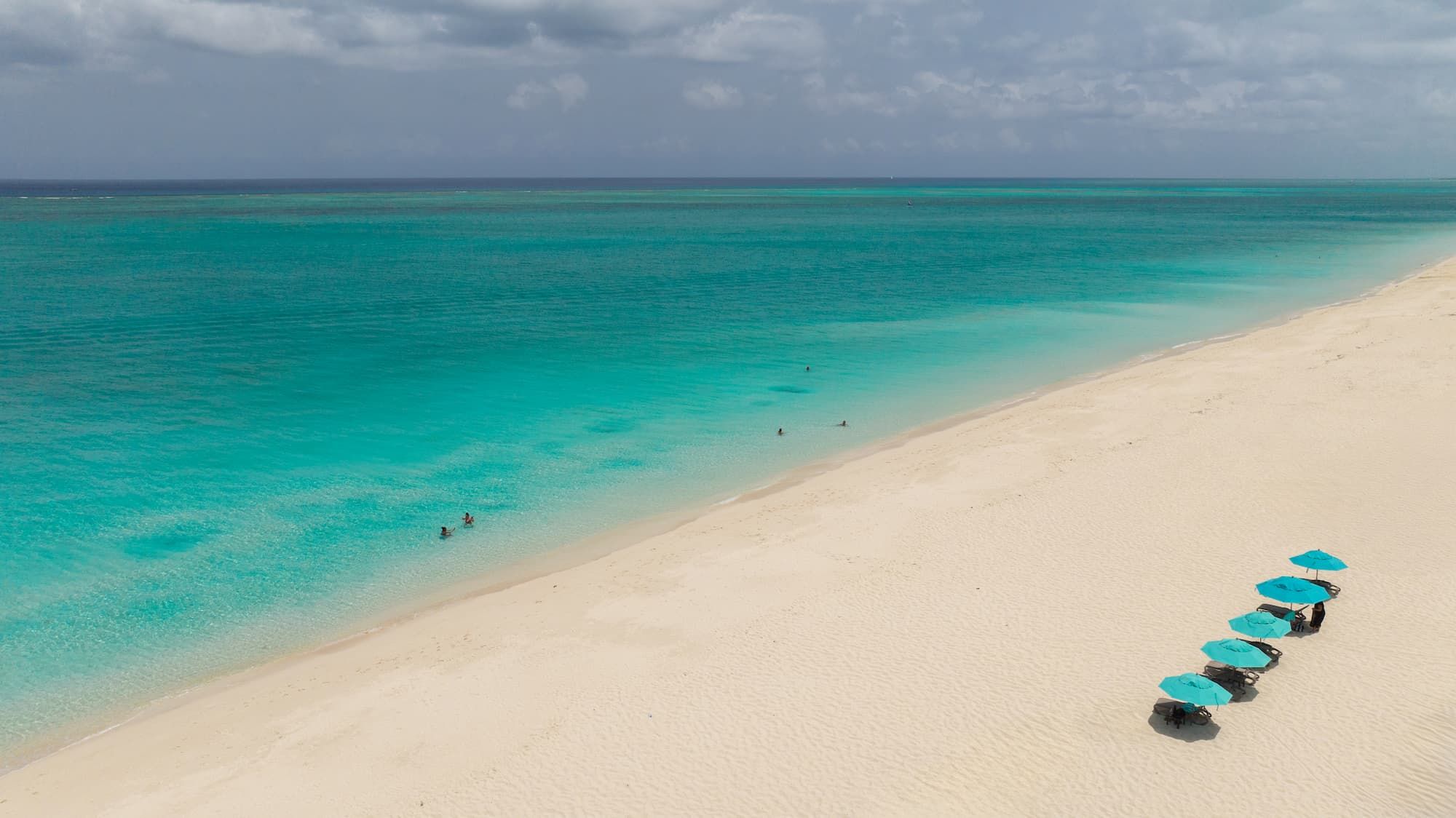 Une plage à l’eau turquoise et limpide, bordée d’une rangée de parasols.