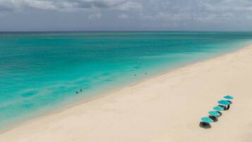 Une plage à l’eau turquoise et limpide, bordée d’une rangée de parasols.