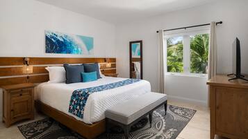 A bedroom with a bed, bedside tables, a bench, a TV stand, and a window with a view of greenery.