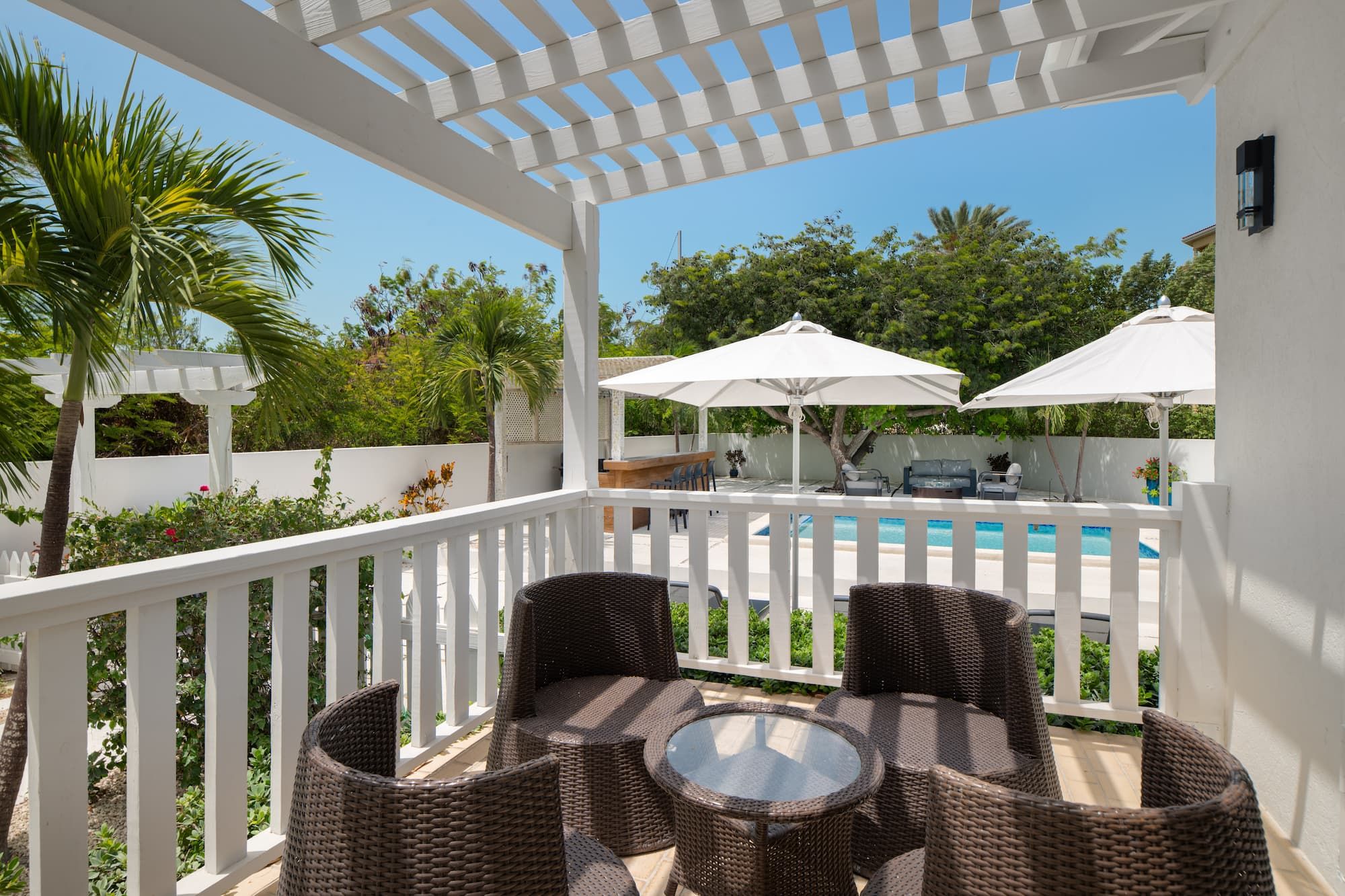 A covered outdoor seating area with wicker furniture and umbrellas, overlooking a swimming pool.