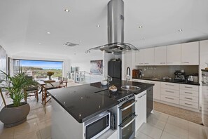 A modern kitchen with a central island, stainless steel appliances, and a view to the outside. - 3 bedroom townhouse with pool and sea views (Warrnambool)