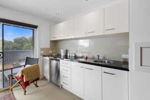 A modern kitchen with white cabinets, a black countertop, and a stainless steel dishwasher. - 3 bedroom townhouse with pool and sea views (Warrnambool)