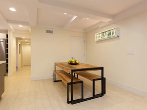 A dining area with a wooden table and benches, a fruit bowl on the table, and a wall-mounted sign. - Ocean Front Oasis (San Diego)
