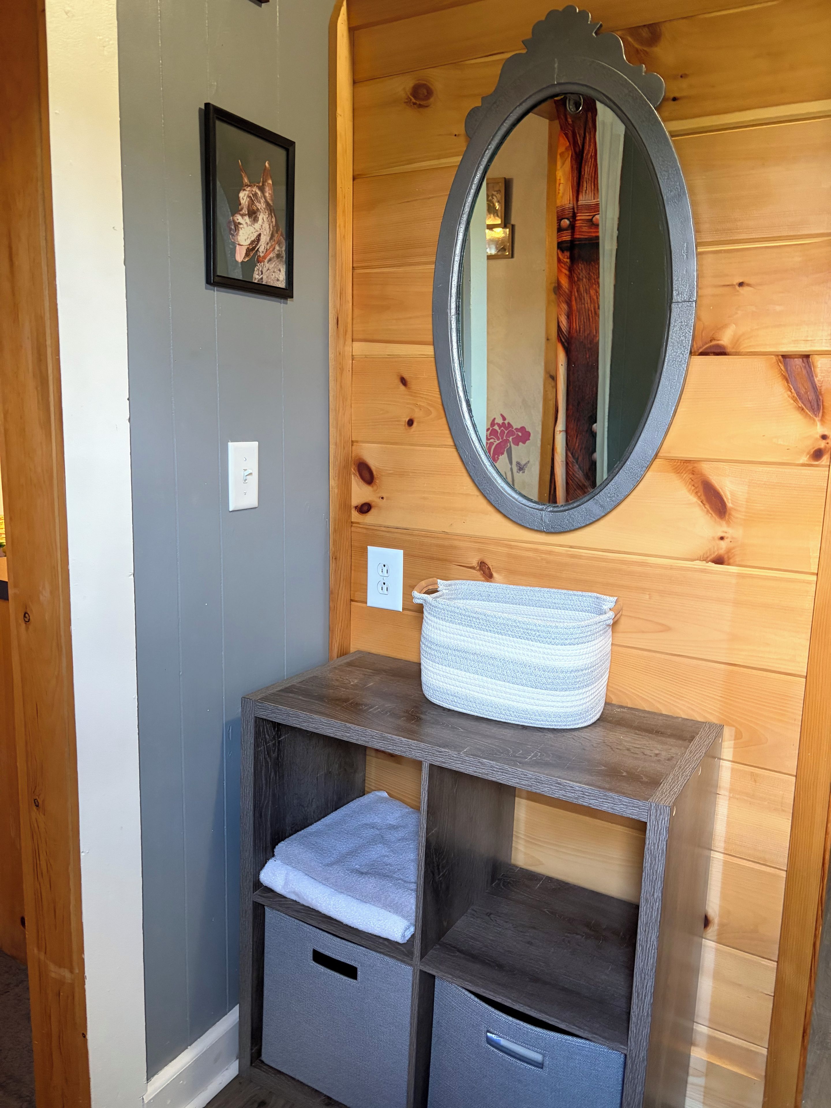 A wooden cabin interior with a mirror, a framed picture, and a woven basket on a dresser.