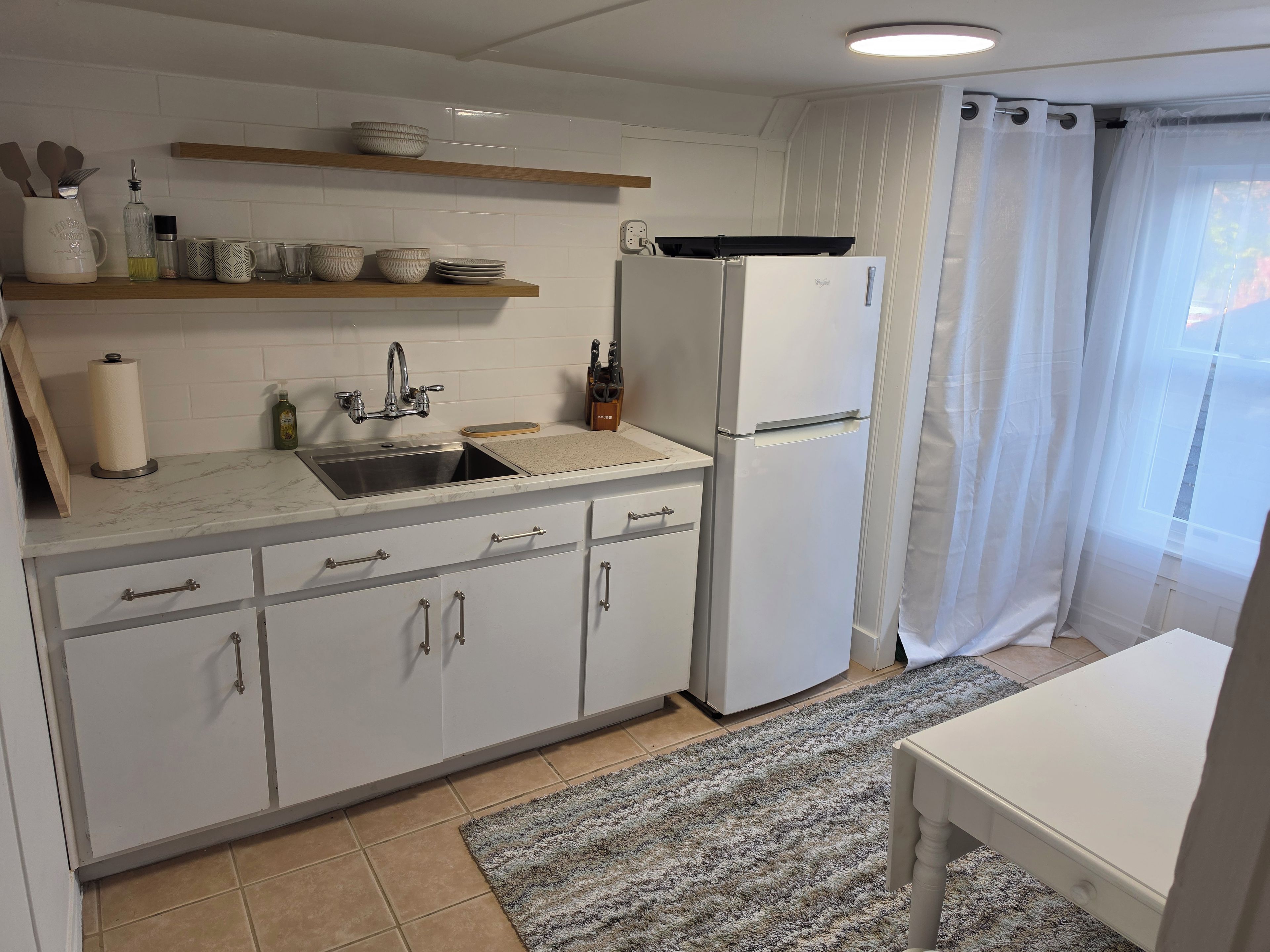 Ett kök med en diskho, ett kylskåp och ett fönster med gardiner.