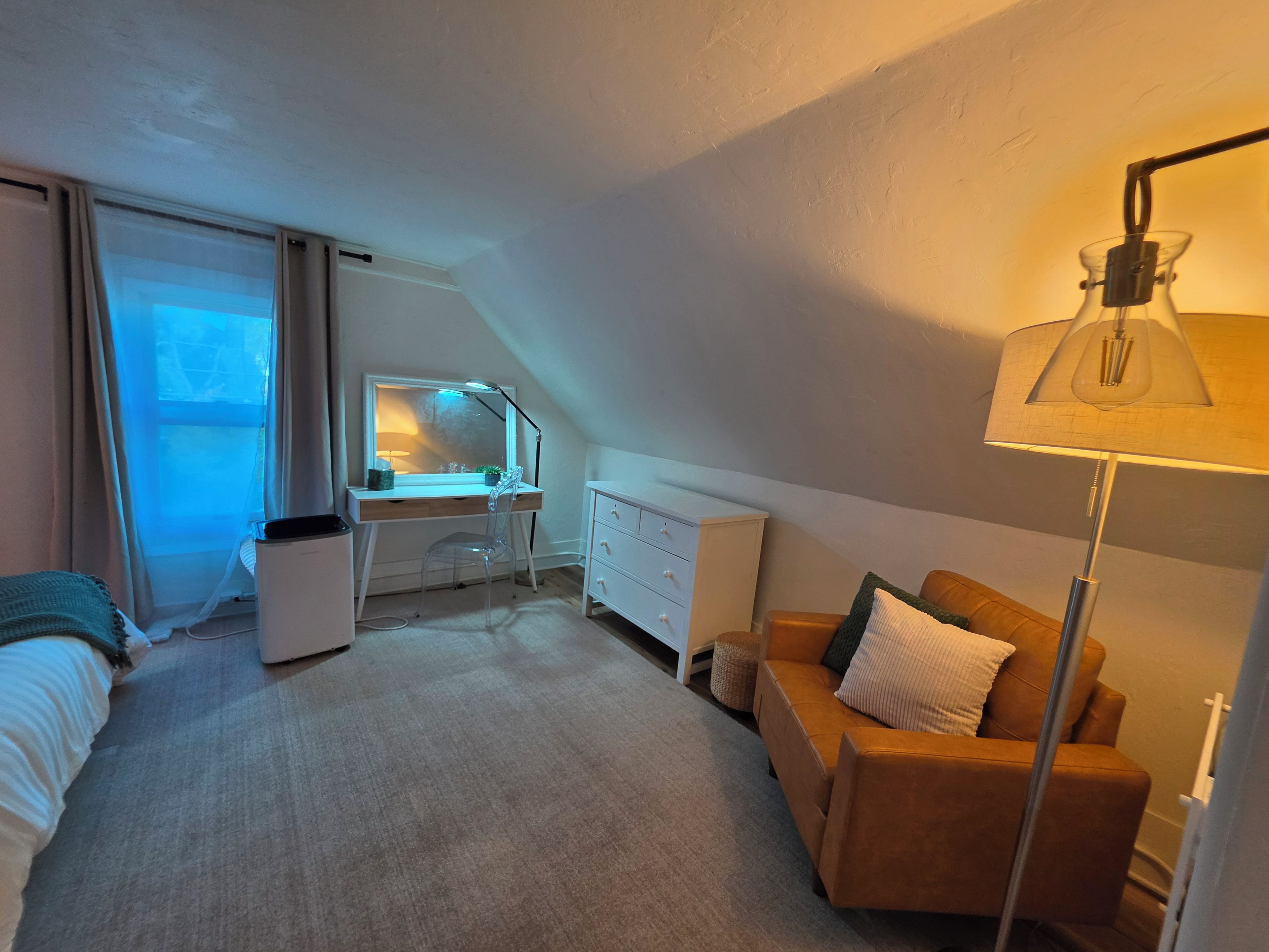 Een slaapkamer met een bureau, een stoel, een bed, een bank, een lamp en een raam.