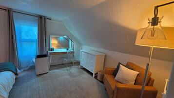 Een slaapkamer met een bureau, een stoel, een bed, een bank, een lamp en een raam.