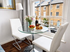 A modern room with a glass table, white chairs, a vase of flowers, a bottle of champagne, and a plate of fruit and pastries. - Islington Gem Studio near Angel and Highbury (London)