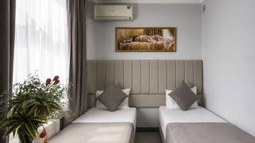 A hotel room with two beds, a dining table, and a painting on the wall.
