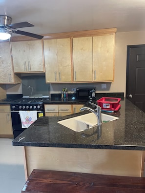 A kitchen with wooden cabinets, a black countertop, a stainless steel sink, a microwave, and a red basket. - Amazing 3-bedroom condo in Playas de Rosarito near the beach. (Playas de Rosarito)